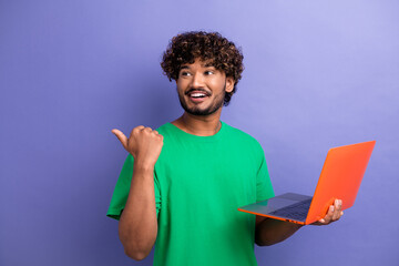 Young man in vibrant green shirt holding orange laptop with cheerful expression and pointing...