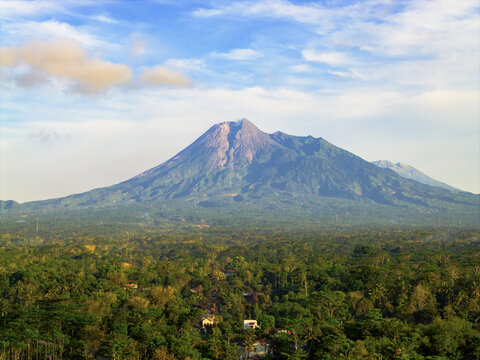 Aerial view of Mount Merapi rises majestically, its slopes draped in emerald forests beneath a vibrant sky, a stunning contrast of earth and sky, Klaten, Central Java, Indonesia.