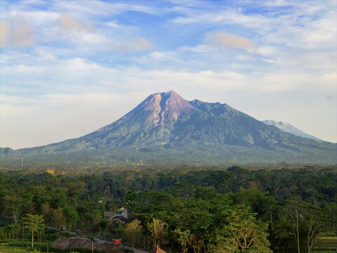 Aerial view of Mount Merapi's majestic peak piercing through a sea of emerald forests under a vibrant sky, Klaten, Central Java, Indonesia.