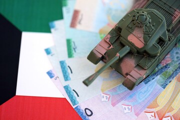 Kuwaiti dinar currency money bills and toy tank on flag close up. The concept of army funds and weapons sales