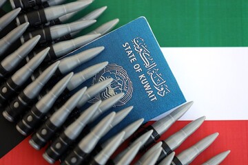Kuwaiti passport and rifle bullets on flag close up. The concept of warfare and gun selling