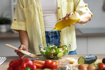 Young woman seasoning the salad with oil in the kitchen at home.