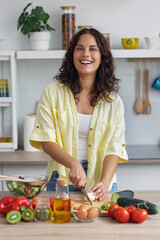 Pretty woman cutting fresh vegetables while preparing healthy salad in the kitchen at home.