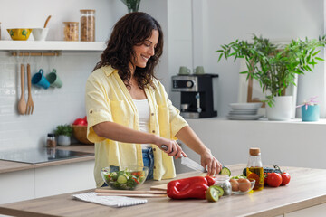 Pretty woman cutting fresh vegetables while preparing healthy salad in the kitchen at home.