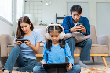 Asian family members immersed in separate digital devices, showing a modern lifestyle and challenge of screen time at home