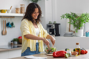 Pretty woman preparing healthy salad in the kitchen at home.