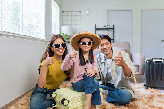 Asian family smiling, giving thumbs up, and preparing for an exciting summer vacation trip with suitcases at home