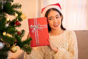 Young Woman with Santa Hat Holding Christmas Gift Next to Christmas Tree Indoor Festive Holiday Season Celebration Xmas Present Giving Happiness