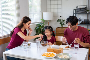 Asian family enjoying a meal together at the dining table. Mother feeding her daughter, father eating next to them