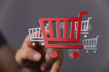Hand reaching out to touch a red shopping cart symbol, representing online shopping, sales,...