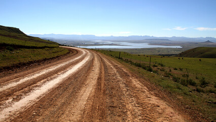 Dirt roads in the QwaQwa villages, located in the mountainous region of the Free State province in South Africa. Trees and plants like Wild Dagga in the foreground. Mountains in the background. 