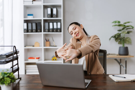 Asian businesswoman doing office stretches at her desk, feeling relaxed during a busy workday or break