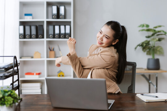Woman smiling, stretching arms at office desk during work break. Concept of employee wellness, healthy lifestyle, stress relief