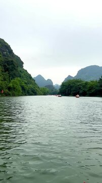 Vertical 4K video of a quiet boat trip on the Trang An river in Ninh Binh surrounded by beautiful mountains and lush greenery outdoor at daytime in Vietnam while traveling in Asia.