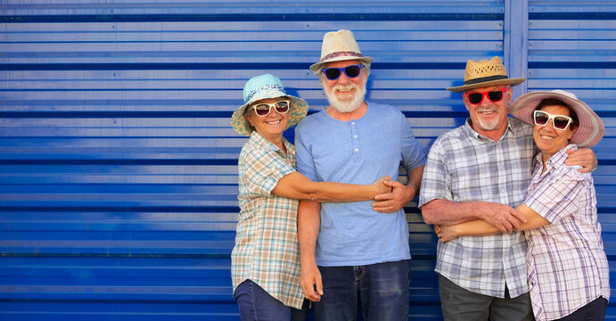 Group of happy senior friends enjoying time together outdoors, smiling and hugging in front of a blue metal wall. Concept of friendship, fun, active lifestyle, and positive aging