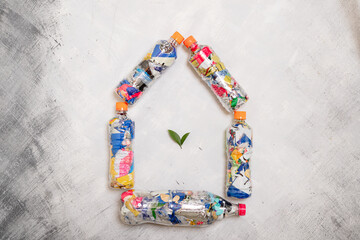 Five pet plastic bottles filled with compressed plastic waste arranged in the shape of a house with green leaves inside
