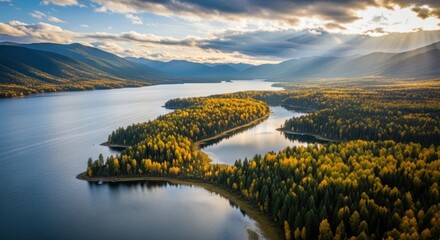 Aerial view of a winding lake surrounded by autumn forest with sun rays breaking through clouds