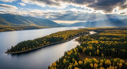Aerial view of a winding river flowing through a lush forest with mountains in the background under a dramatic sky