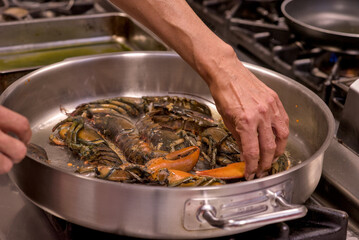 Close-up of chef’s hands cooking fresh seafood in a stainless steel pan over a gas stove in a professional industrial kitchen. Visible steam and warm light emphasize the freshness and craftsmanship of