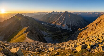 Golden sunrise illuminates rugged mountain range with deep valley and clear blue sky