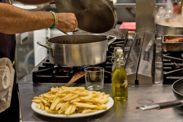 Chef cooking at industrial stove with potatoes and olive oil