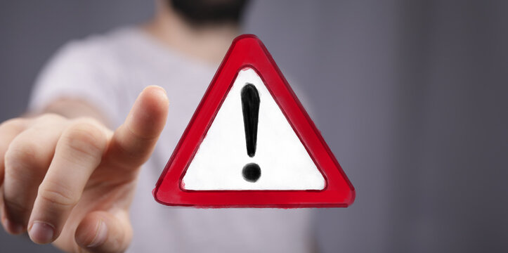 Urgent warning concept.  Hand interacts with a red triangle alert symbol. Stock photo for website, blog, and social media.