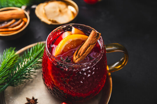 Holiday Mulled Wine with Orange and Apple in glass Mug Surrounded by Christmas Decor on black background close up