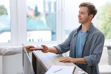 Receptionist giving passport and hotel key card to guest at reception desk indoors, closeup