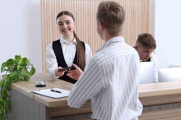 Receptionist giving passport and hotel key card to guest at reception desk indoors