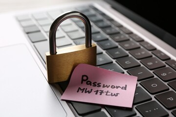 Paper note with password and closed padlock on laptop, closeup