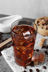 Tasty coffee with ice in glass, beans, milk and sugar cubes on wooden table against grey background, closeup
