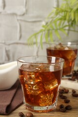 Tasty coffee with ice in glasses and beans on wooden table against light textured background, closeup