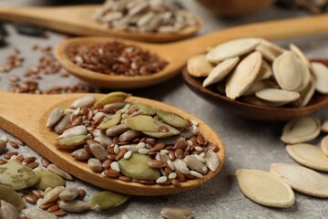 Different seeds in spoons on grey table, closeup