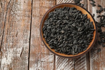 Sunflower seeds in bowl on wooden table, top view. Space for text