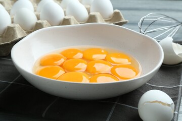 Raw eggs, yolks in bowl and whisk on table, closeup