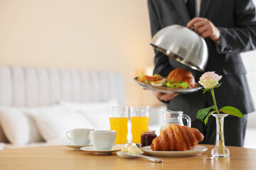 Waiter serving breakfast on wooden table in hotel room, closeup. Space for text