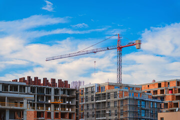 Construction site with modern apartment buildings under development and tower crane against blue sky. Concept of urban growth, real estate investment, infrastructure growth, residential construction