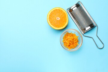 Orange zest, fresh fruit and grater on light blue background, flat lay. Space for text
