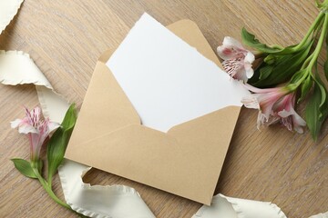 Envelope with blank card and flowers on wooden table, flat lay. Mockup for design