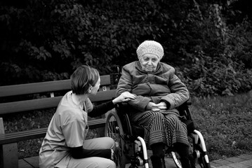 Elderly woman in wheelchair with healthcare worker in blue uniform outside in park