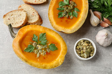 Tasty pumpkin cream soup with seeds, parsley, garlic and bread on grey textured table, flat lay