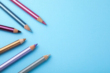 Eye pencils on light blue background, flat lay. Space for text
