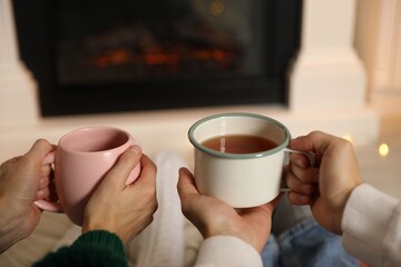 Couple with cups of hot tea resting near fireplace at home, closeup
