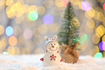 Cute decorative snowman on artificial snow against blurred lights, closeup