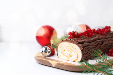 Delicious Yule log (traditional Christmas cake) with redcurrant, decor and fir tree branches on light table, closeup. Space for text