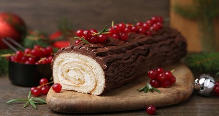 Delicious Yule log (traditional Christmas cake) with redcurrant on wooden table, closeup