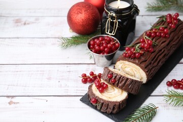 Delicious Yule log (traditional Christmas cake) with redcurrant, decor and fir tree branches on light wooden table, closeup. Space for text