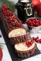 Delicious Yule log (traditional Christmas cake) with redcurrant on light table, closeup