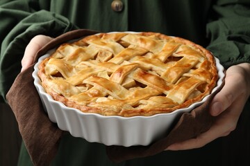 Woman with baking dish of delicious homemade apple pie against dark background, closeup