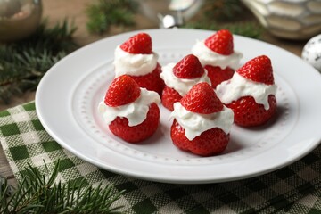 Christmas food. Santa hats made of strawberries, whipped cream and decor on table, closeup